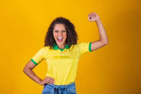 Photo for Brazil supporter. Brazilian curly hair woman fan celebrating on soccer, football match on yellow background. Brazil colors. - Royalty Free Image