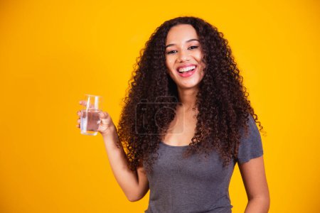 Téléchargez les photos : Belle afro femme eau potable sur fond jaune avec espace pour le texte. - en image libre de droit
