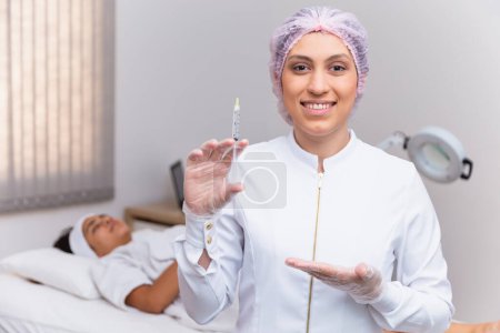 Photo for Woman applying hyaluronic acid on her face. Beautician holding a syringe with hyaluronic acid and patient in the background. - Royalty Free Image