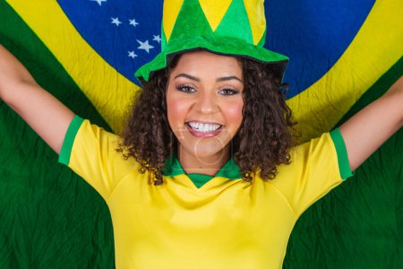 Foto de Afro niña animando a la selección brasileña favorita, sosteniendo la bandera nacional en el fondo amarillo
. - Imagen libre de derechos
