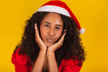 Foto de Primer plano de la mujer afro vistiendo Santa Claus sombrero labios puckering puching o soplando besos sobre fondo amarillo - Imagen libre de derechos