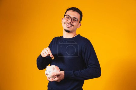 Photo for Businessman saving money by putting coins in piggy bank. Young boy with piggy bank depositing coins - Royalty Free Image