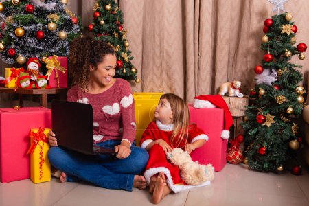 Téléchargez les photos : Famille mère et enfant fille utilisent ordinateur portable à la maison pendant les vacances de Noël. - en image libre de droit