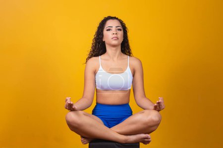 Foto de Gente, concepto de paz y meditación. Mujer joven afro tranquila practica yoga sobre fondo amarillo. - Imagen libre de derechos