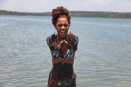 Téléchargez les photos : Jeune femme afro se baignant dans l'argile naturelle dans la rivière. - en image libre de droit