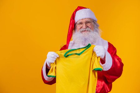 Photo for Santa Claus is a fan of Brazil. Santa Claus supporter of the Brazilian team. Sports championship. Santa Claus holding the team shirt. Soccer match. - Royalty Free Image