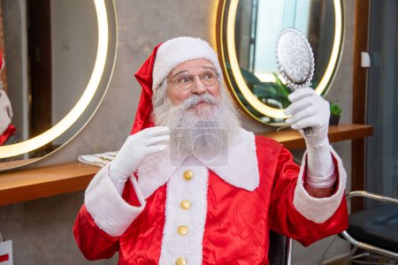 Téléchargez les photos : Le vrai Père Noël dans le salon de coiffure tenant un miroir se regardant lui-même. - en image libre de droit