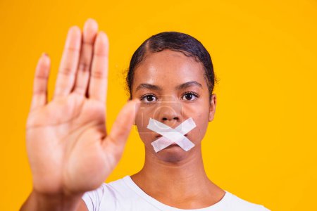 Photo for Black woman on yellow background with her mouth closed in silence. Concept of prejudice, abuse and racism - Royalty Free Image