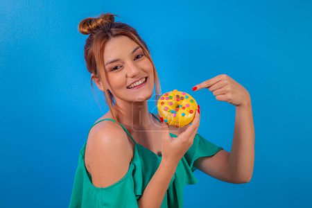 Foto de Chica pelirroja con rosquilla amarilla y confeti colorido sobre fondo azul. - Imagen libre de derechos