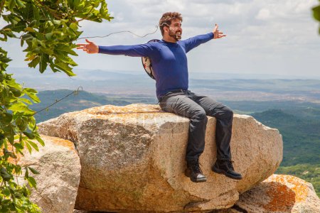 Foto de Hombre con los brazos abiertos sentado en la roca en una montaña. Concepto de aventura y victoria - Imagen libre de derechos