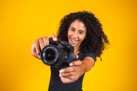 Téléchargez les photos : Jeune afro femme photographie sur fond jaune tenant un appareil photo. jeune femme photographies - en image libre de droit