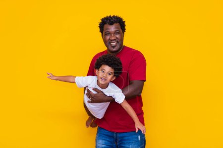 Téléchargez les photos : Père et fils afro sur fond jaune souriant et jouant. Concept de fête des pères - en image libre de droit
