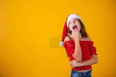 kleines Mädchen, das weihnachtlich gekleidet ist und mit dem Daumen auf freien Platz für Text zeigt. Aktionen und Kampagnen zum Jahresende