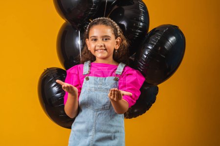 Téléchargez les photos : Petite fille souriante avec des ballons noirs le vendredi noir. festival à bas prix - en image libre de droit