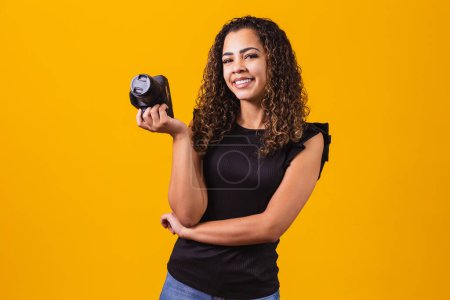 Foto de Joven mujer afro fotografía sobre fondo amarillo sosteniendo una cámara fotográfica. - Imagen libre de derechos