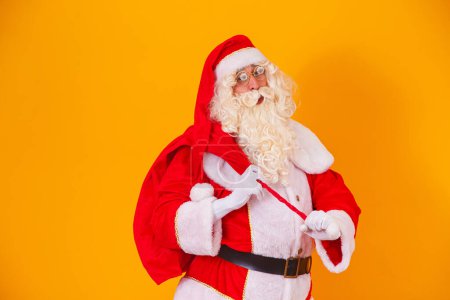 Foto de Santa Claus con una bolsa enorme en la prisa para entregar regalos de Navidad. Santa Claus sobre fondo amarillo - Imagen libre de derechos