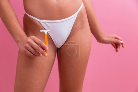 Foto de Primer plano de una chica en bragas blancas sosteniendo una hoja de afeitar amarilla en sus manos sobre un fondo rosa. - Imagen libre de derechos
