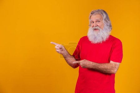 Photo for Old man with a long beard pointing to the side on a yellow background. Senior with white beard. - Royalty Free Image