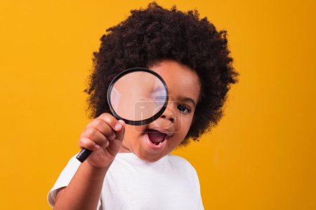 Téléchargez les photos : Enquête, découverte et concept de vision - heureuse petite afro-américaine regardant à travers la loupe sur fond jaune - en image libre de droit