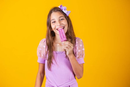 Téléchargez les photos : Une petite fille qui mange une glace glacée. Adorable petite fille avec délicieuse crème glacée sur fond de couleur - en image libre de droit
