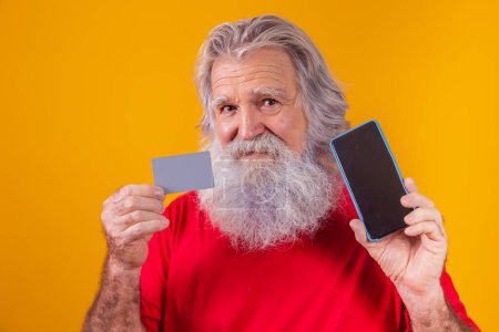 Téléchargez les photos : Portrait d'un beau Père Noël tenant carte de crédit et smartphone avec écran vierge pour le texte dans sa main. - en image libre de droit