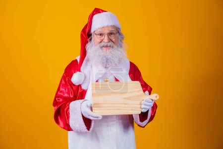 Photo for Santa Claus dressed in apron holding empty meat board on yellow background. - Royalty Free Image