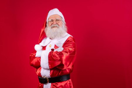 Photo for Santa Claus crossed arms on red background. Kind bearded Santa Claus with arms folded over red background. Studio shot of realistic Santa Claus. - Royalty Free Image