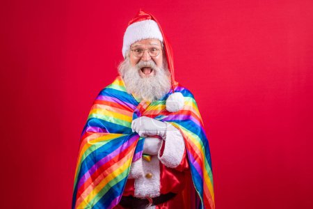 Photo for Santa Claus covering with LGBT pride flag. By myself. One. Keeping your fist up, covering the LGBT flag. LGBT + flag on red background. Xmas. - Royalty Free Image