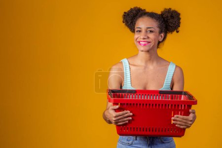 Téléchargez les photos : Souriant afro femme tenant panier vide regardant la caméra souriant - en image libre de droit
