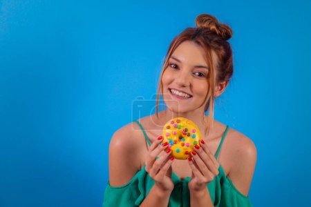 Photo for Red-haired girl with yellow donut and colorful confetti on blue background. - Royalty Free Image