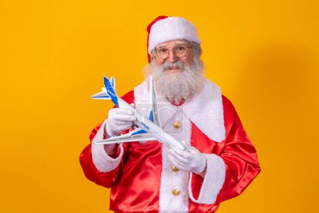 Foto de Santa Claus sostiene un pequeño avión de juguete sobre fondo amarillo. Concepto de viaje de Navidad - Imagen libre de derechos