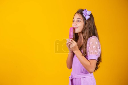 Téléchargez les photos : Petite fille mangeant une glace glacée colorée en été. Fille tenant une glace éclatante - en image libre de droit