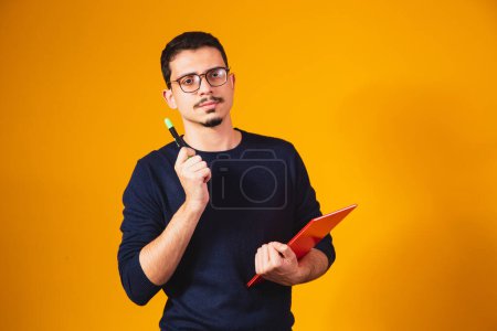 Téléchargez les photos : Portrait de garçon étudiant pensant et tenant un carnet sur fond jaune. - en image libre de droit
