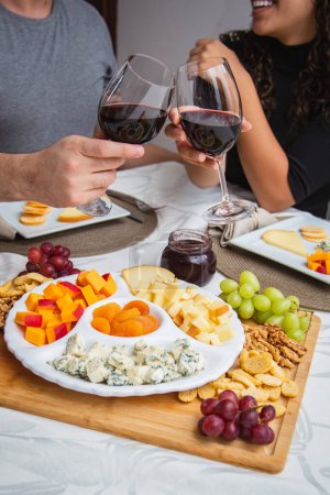 Photo for Couple toasting with wine and cheese at dinner. Focus on cheeses - Royalty Free Image