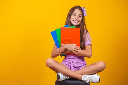 Téléchargez les photos : Petite étudiante fille avec des cahiers dans les mains assis - en image libre de droit