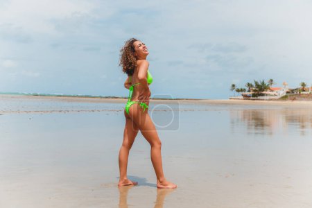 Foto de Hermosa mujer afro brasileña en una playa en rio grande do norte, sonrió, sintiendo la libertad y las olas del mar, disfrutando de sus vacaciones de verano con un maravilloso sol y calidez - Imagen libre de derechos