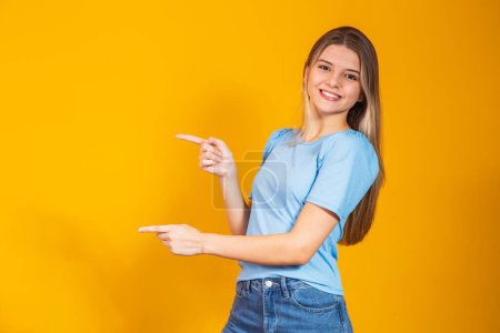 Photo for Caucasian smiling young woman pointing with two fingers to the side with free space for text. - Royalty Free Image