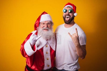 Téléchargez les photos : Garçon à côté du Père Noël faisant rock in roll signe. Père Noël est un rocker - en image libre de droit