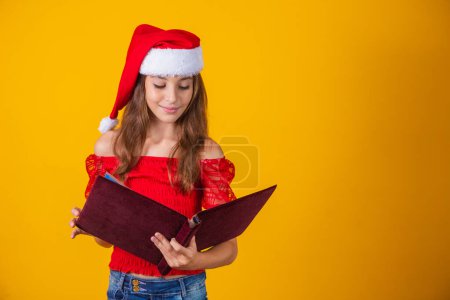 Foto de Hermosa niña caucásica con un libro rojo aterciopelado leyendo historias de Navidad. - Imagen libre de derechos