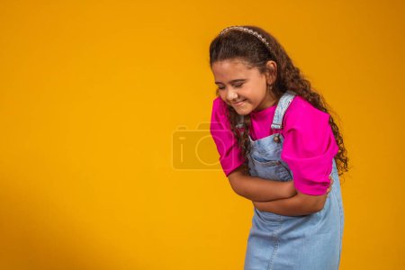 Photo for A girl on a yellow background has a stomachache. Holding hands on belly and suffering. - Royalty Free Image