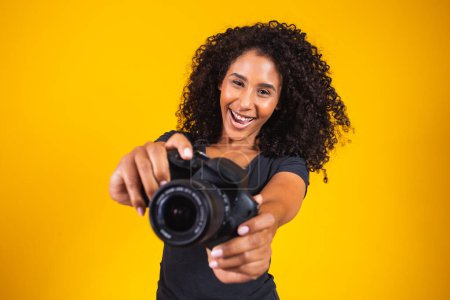 Foto de Joven mujer afro fotografía sobre fondo amarillo sosteniendo una cámara fotográfica. fotografías de mujer joven - Imagen libre de derechos