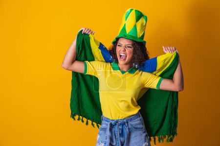Photo for Afro girl cheering for favorite brazilian team, holding national flag in yellow background. - Royalty Free Image