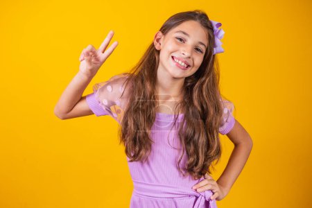 Photo for Photo of a charming and delicate preteen girl making a V sign smiling isolated on yellow background. - Royalty Free Image