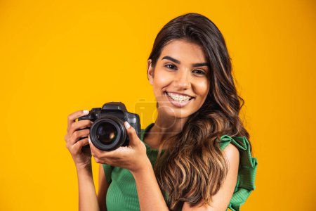 Photo for Young girl holding a photo camera on yellow background. woman taking picture - Royalty Free Image