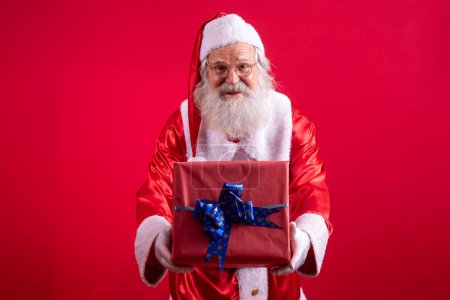 Téléchargez les photos : Père Noël tenant un cadeau de Noël sur fond rouge. - en image libre de droit