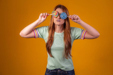 Foto de Joven mujer pelirroja con coloridas piruletas vendando los ojos. concepto de moda - Imagen libre de derechos