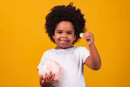 Photo for Little girl saving money in a piggybank on yellow background - Royalty Free Image