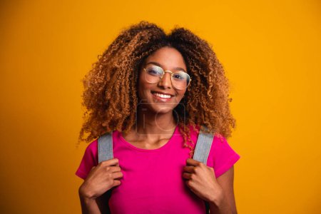 Photo for Young afro with backpack on his back on yellow background. Young student smiling with glasses - Royalty Free Image
