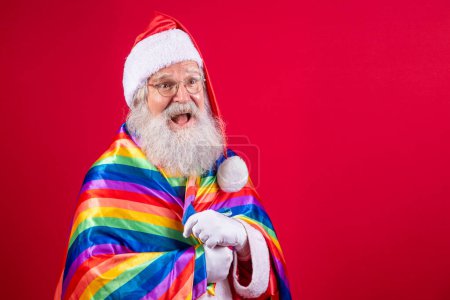 Photo for Santa Claus covering with LGBT pride flag. By myself. One. Keeping your fist up, covering the LGBT flag. LGBT + flag on red background. Xmas. - Royalty Free Image