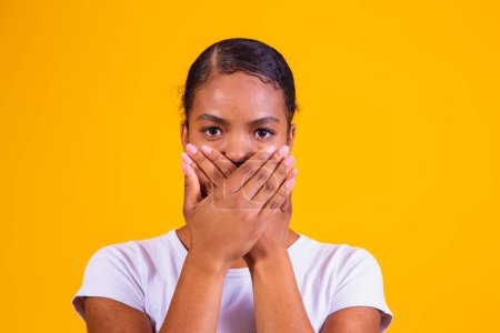 Foto de Mujer negra sobre fondo amarillo con la boca cerrada en silencio. Concepto de prejuicio, abuso y racismo - Imagen libre de derechos